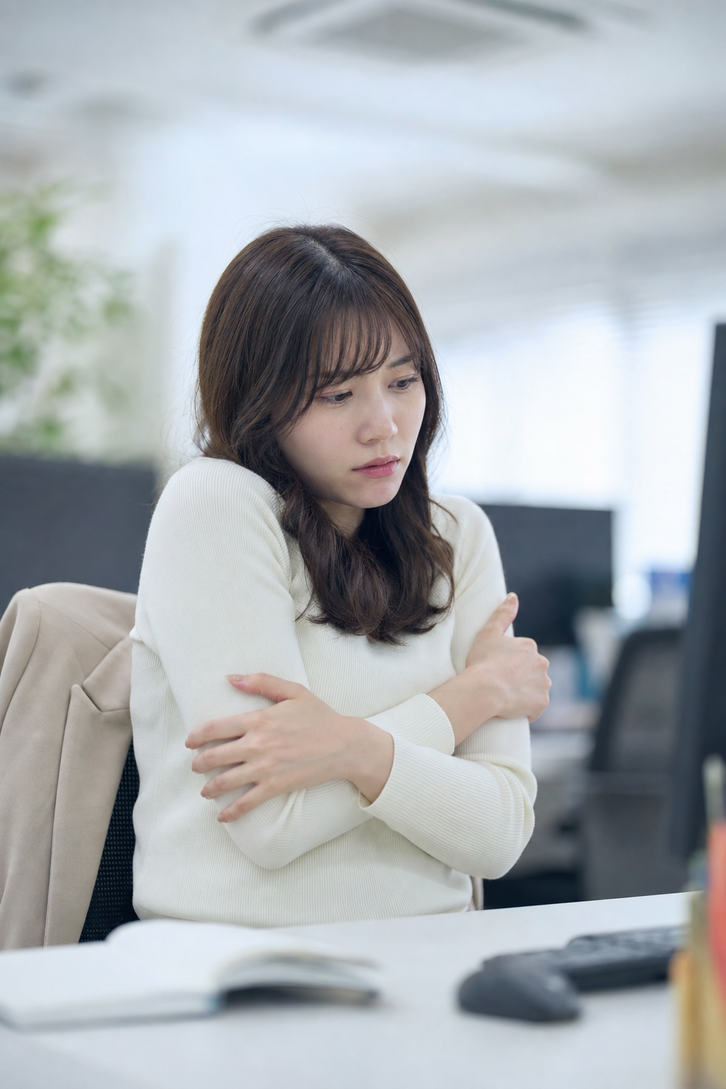 夏のオフィスで冷房により体が冷えて肩や腕をさする女性の様子