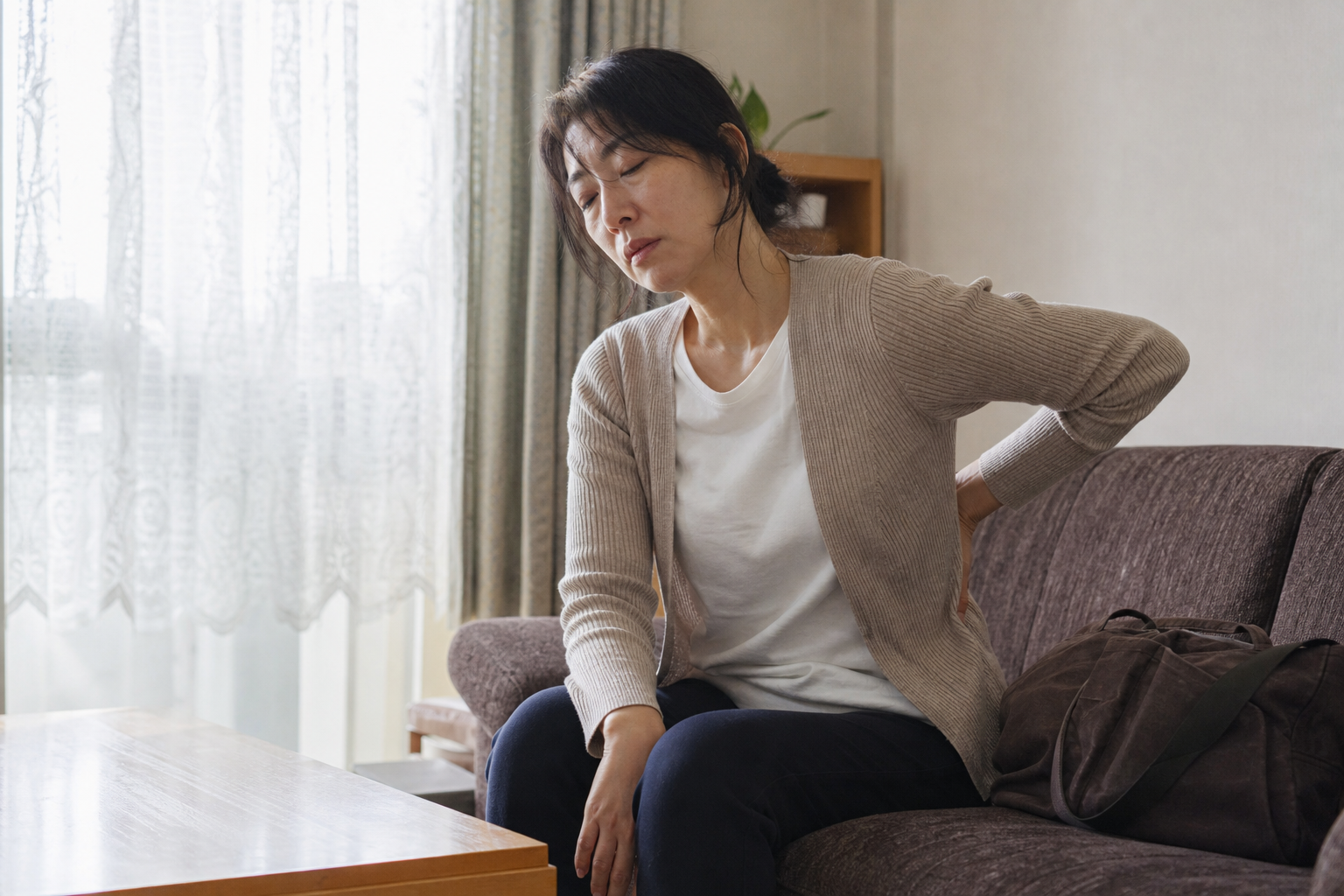 夜勤明けの朝に自宅のソファで疲れた表情のまま座り込む40代の女性看護師
